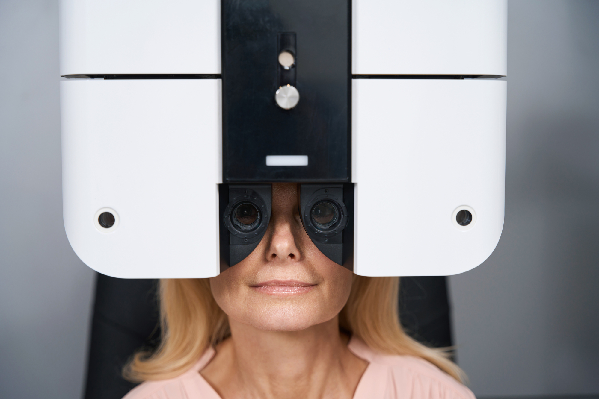 Portrait of lady sitting on chair and looking through special ophthalmic device at the camera in hospital